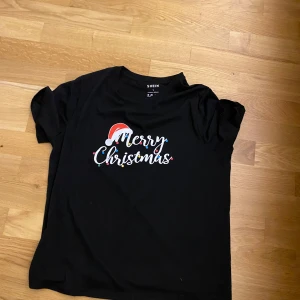 Svart jul-tshirt från SHEIN - Svart t-shirt från SHEIN med trycket 'Merry Christmas' i vitt. Rund hals och korta ärmar. Tröjan är lite smutsig på bilden men jag kommer tvätta den. Säljer den för den var för stor. SUPER BILLIG!!!!!!