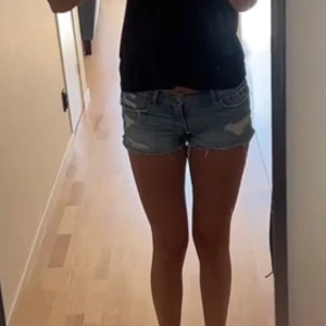 Abercrombie & Fitch  jeansshorts - Säljer ett par ljusblå jeansshorts från Abercrombie & Fitch med råa kanter och slitna detaljer både fram och bak. Shortsen har klassiska fickor, knapp och dragkedja samt låg midja. Perfekta för chill sommardagar och har en loose passform. I stl w26