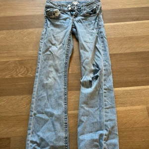 Ljusblå jeans från Gina Tricot - Säljer ett par ljusblå jeans från Gina Tricot i storlek 152. Modellen har raka ben och ett snyggt hål på ena knät för en cool, avslappnad vibe. Klassisk femficksdesign och knappgylf. Perfekta för dig som gillar streetstyle och vill sticka ut.