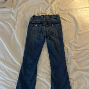 Blå bootcut jeans från Grunt, stl 26 - Säljer ett par blå bootcut jeans från Grunt i modellen Alabama Low Flare Blue, Jeansen har låg midja.