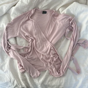 Rosa omlottopp från Gina Tricot - Säljer en söt rosa omlottopp från Gina Tricot. Toppen har långa ärmar och knytband i midjan för en justerbar passform. Ändast testad