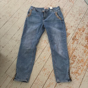 Blå jeans från Mos Mosh med detaljer - Snygga blå jeans från Mos Mosh med coola broderade detaljer vid fickorna och dragkedja vid benslut. Modellen har klassisk femficksdesign och raka ben med något smalare passform. Perfekta för dig som gillar stilrena jeans med en twist.
