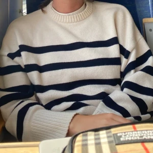 Randig tröja i krämvit och marinblå - Säljer en stilren randig tröja i krämvit och marinblå. Tröjan har en avslappnad passform och är perfekt för en casual look. Den är långärmad och gjord i ett mjukt material som känns skönt mot huden.