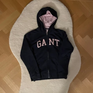 Marinblå zip-up från GANT (164) - Snygg marinblå hoodie från GANT stor gant logan skrivit på tröjan . Perfekt för en avslappnad stil med dragkedja framtill och praktiska fickor. Storleken är 13-14 år/ 164 cm.