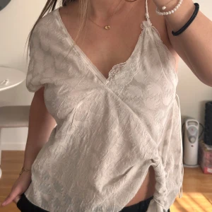 Vit omlottlinne med spetsdetaljer - Säljer ett stilrent vitt omlottlinne med spetsdetaljer. Linnet har en v-ringad design och tunna band. Aldrig använd med lapp kvar!! Storlek m, nypris 399 säljer för 200