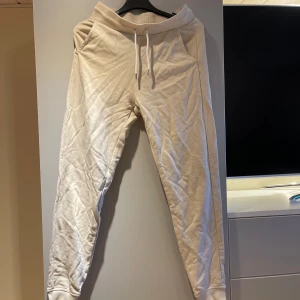 Beige mjukisbyxor från GANT - Snygga beige mjukisbyxor från GANT i storlek XS. Byxorna har en ribbad midja med snörning och fickor på sidorna. Perfekta för en avslappnad stil.