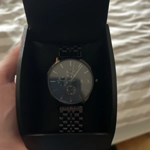 Svart klocka från Armani  - Snygg svart klocka från Armani Exchange med stilren design. Klockan har en svart urtavla med diskreta markeringar och en länkarmband i metall. Perfekt för den som gillar en elegant och modern stil. Priset är inte hugget i sten!