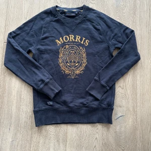  Sweatshirt från Morris - Säljer en snygg mörkblå sweatshirt från Morris med ett guldtryck på framsidan. Storlek XS. Mycket bra skick. Tröjan har långa ärmar och ribbade muddar vid ärmslut och nederkant. Perfekt för en avslappnad stil.