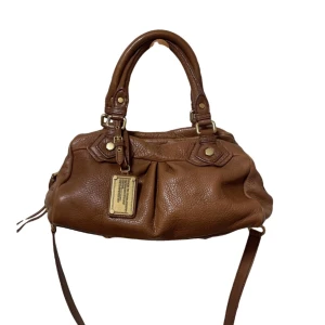 Marc jacobs väska brun  - Classic Q-väska, baby groove modell. Något tecken på användning men i väldigt bra skick (t.ex. bild nr 4 lite repig i dragkedja). Bredd: 31cm, Höjd: 18cm, Djup: 18cm. Läder material. Köpt från Vestiare collective med godkänd autentisering & kvalitetskontroll, kan skicka bild. 