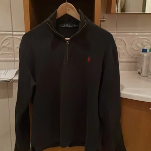 Grå tröja med dragkedja från Ralph Lauren - Säljer en stilren grå tröja från Ralph Lauren med en halv dragkedja och det klassiska röda logotypbroderiet på bröstet. Tröjan har långa ärmar och en hög krage, perfekt för kyligare dagar. Priset är inte hugget i sten så kom gärna dm! 