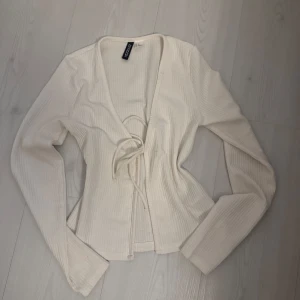 Vit ribbad topp från H&M Divided - Säljer en stilren vit ribbad topp från H&M Divided. Toppen har långa ärmar och en knytning framtill som ger en snygg detalj! 💕