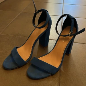 Blå klackskor med ankelrem - Blå klackskor med remmar och justerbar ankelrem. Skorna har en blockklack som är 10cm hög.