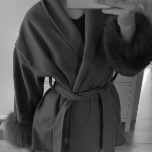 Elegant kappa med pälsdetaljer - Snygg kappa med bälte och pälsdetaljer vid ärmslut. Perfekt för kyligare dagar med sin stilrena design och bekväma passform. Ett måste för garderoben!