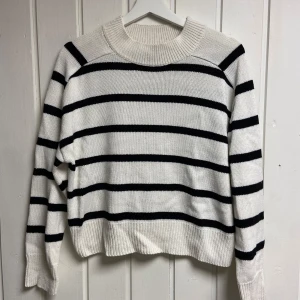 Vit  svart randig stickad tröja - Vit stickad tröja med svarta ränder. Tröjan har långa ärmar och en rund halsringning.