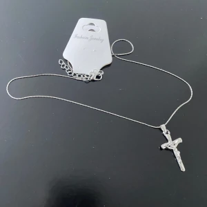 925 Silverpläterade Korsband  - Elegant silverfärgat halsband med ett korshänge. Perfekt för att lägga till en subtil och stilren detalj till din outfit. Kedjan är tunn och justerbar för att passa olika längder.