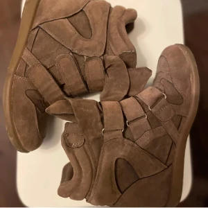 Bruna sneakers med kilklack - Snygga bruna sneakers i mocka med kilklack och kardborreband. De liknar isabel marant skorna!! De är knappt använda och otroligt fina. Säljer då jag inte använder dom! Köpta för 800kr säljer för 450kr! Hör av er vid frågor!❤️storlek 39 men passar mig som brukar ha 38!