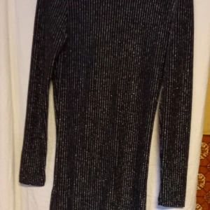 Läcker svart glittrig klänning - Snygg läcker svart glitterklänning med glittriga silverdetaljer. Den har en åtsittande passform och långa ärmar, perfekt för en kväll ute. Materialet består av polyamid, metallfibrer och elastan vilket ger en stretchig och bekväm känsla.