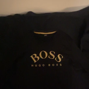 Svart t-shirt från Hugo Boss - Snygg svart hoodie från Hugo Boss med stort BOSS-tryck på framsidan. Perfekt för en stilren look. Den säljs inte längre! Och är förväntan tröja, nypris 1799!