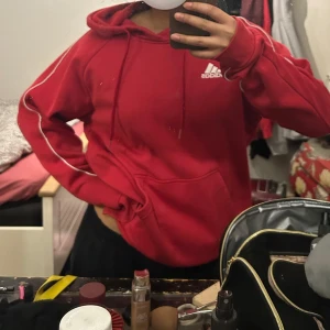Röd hoodie från Adidas - Säljer en snygg röd hoodie från Adidas. Den har en klassisk design med känguruficka och justerbar huva. Perfekt för en avslappnad stil. Använd fåtal gånger. 