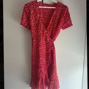 Röd prickig klänning - Charmig röd klänning med vita prickar och omlott-design. Aldrig använd, så i nyskick. Strolek:S🩷🫶🏼