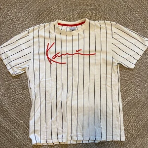 Vit randig t-shirt från Karl Kani - Säljer en vit t-shirt från Karl Kani med svarta ränder och röd logga på bröstet. 