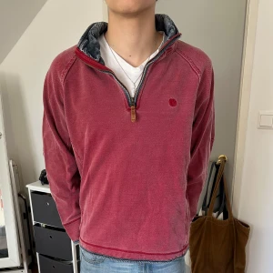 Röd tröja med dragkedja - Säljer en röd tröja med dragkedja och hög krage. Tröjan har långa ärmar och en liten broderad detalj på bröstet. Perfekt för en avslappnad stil.