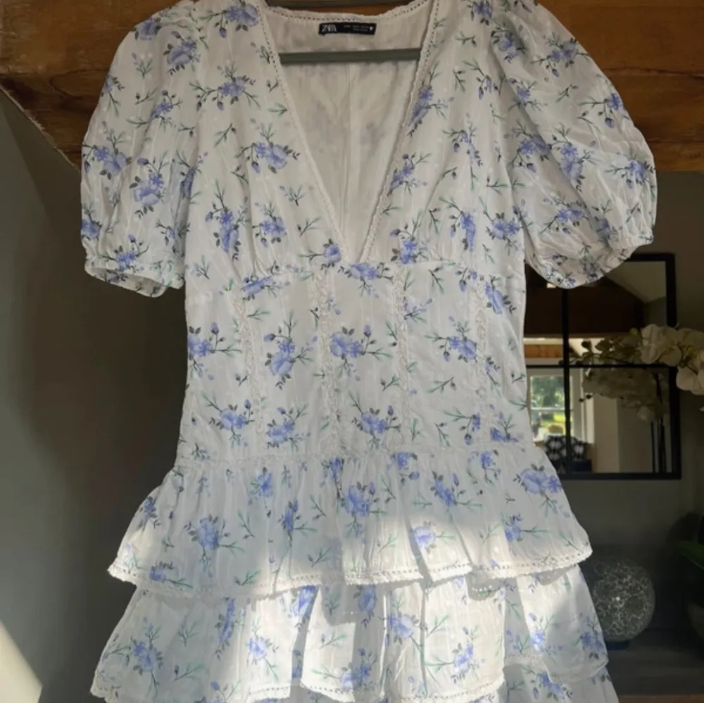 Söt blommig klänning från Zara i vitt med blå och gröna blommor. Klänningen har korta ärmar och volanger, samt en v-ringad design med spetsdetaljer. Perfekt för sommarens alla tillfällen! Har aldrig använt, helt ny. Kan inte skicka förens 19e mars men kan reservera. (This dress has been reserved to a buyer for 700sek!! Don’t send offers below . Mekot.