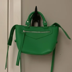 Grön axelväska med dragkedja - Snygg grön axelväska i syntetmaterial med praktisk dragkedja framtill. Väskan har både handtag och en justerbar axelrem för flexibel användning. Perfekt för att ge en färgklick till din outfit!