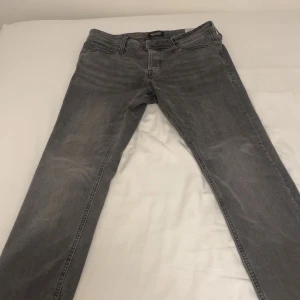 Grå slim jeans från Jack & Jones - Snygga grå slim fit jeans från Jack & Jones, modell Glenn. Perfekta för en stilren look med klassisk femficksdesign och knappgylf. 