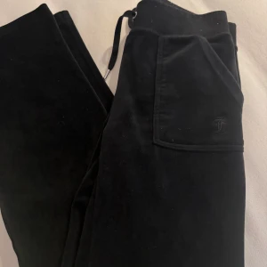Svarta byxor från Juicy Couture - Snygga svarta byxor från Juicy Couture i mjukt sammetstyg. De har en praktisk ficka med knappar och en bekväm midja. Perfekta för en avslappnad stil. Lite noppriga på sömmen men lätt att ta bort.