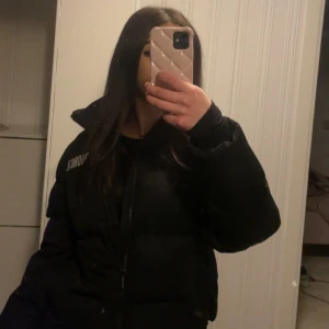 Svart pufferjacka från Hoodrich - Säljer en svart pufferjacka från Hoodrich med märkets logga tryckt på bröstet och ryggen. Jackan har en klassisk pufferdesign med långa ärmar och dragkedja framtill. Säljer eftersom den inte längre används💕