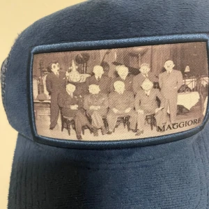 Blå keps med vintage-tryck från Maggiore - Snygg blå keps från Maggiore med ett unikt vintage-tryck på framsidan. Kepsen har ett justerbart band bak och mesh-paneler för ventilation. Perfekt för en avslappnad stil.