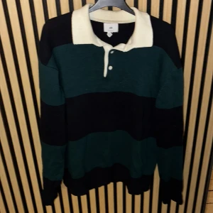 Randig tröja från H&M - Säljer en randig tröja från H&M i grönt och svart med en vit krage. Tröjan har långa ärmar och knappar framtill. Perfekt för en avslappnad stil. Den är storlek S men skulle säga att den är mer som M. Skriv PM för mer information.