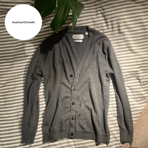 Grå cardigan/kofta från These Glory Days - Säljer en stilren grå kofta från These Glory Days i Superior Merino. Koftan har en v-ringad design med knappar framtill och långa ärmar. Perfekt för en elegant och bekväm look. Skriv vid minsta fråga eller fundering!😊🙌 OBS den har hål kolla bild 5 annars är tröjan användbar