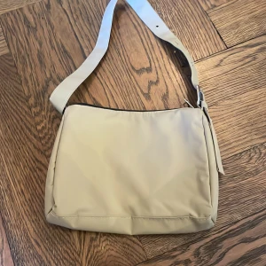 Beige axelväska med dragkedja - Snygg beige axelväska med justerbar rem och dragkedja. Perfekt för att bära dina dagliga nödvändigheter med stil. Enkel och stilren design som passar till många olika outfits.