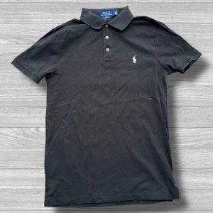 Ralph Lauren piké - Säljer en stilren svart pikétröja från Ralph Lauren med klassisk krage och knappslå. Tröjan har en broderad logotyp på bröstet och är i slim fit. Perfekt för en avslappnad men ändå snygg look.