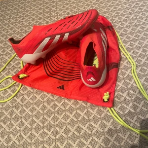 fotbollsskor från Adidas predators  - Snygga röda Adidas fotbollsskor med vita detaljer och dobbar för optimalt grepp på planen. Skorna har en strömlinjeformad design och är perfekta för fotbollsspelare som vill ha både stil och funktionalitet. Skicket är väldigt bra använt i cirka 8/10 gånger! Köptes rätt nyss från unisport.