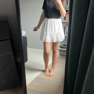 Vit prickig kjol - Söt vit kortkjol med prickigt mönster och volangdetaljer. Perfekt för en somrig look. Elastisk midja för bekväm passform.