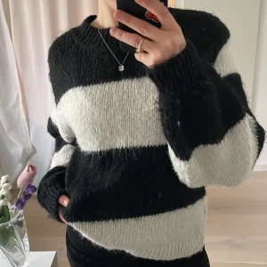 Randig stickad tröja från Gina Tricot - Säljer en mysig stickad tröja från Gina Tricot i svart och vit. Tröjan har breda ränder och långa ärmar, perfekt för kyliga dagar. Den är gjord i ett mjukt material som känns skönt mot huden. Passar bra till både jeans och kjol.