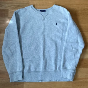 Grå sweatshirt från Ralph Lauren - Säljer en klassisk grå sweatshirt från Ralph Lauren med rund halsringning och broderad logga på bröstet. Perfekt för en avslappnad stil. Tröjan har långa ärmar och är tillverkad i ett mjukt material för extra komfort.