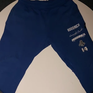 Blå mjukisbyxor från Hoodrich  - Snygga blå mjukisbyxor från Hoodrich med tryck på både fram- och baksida. Byxorna har en bekväm passform och dragkedja vid fickorna. Perfekta för en avslappnad stil.