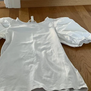 Vit blus med puffärmar från Hm - Säljer en stilren vit blus med puffiga kortärmar. Perfekt för en chic och elegant look. Blusen har en rund halsringning och är tillverkad i ett mjukt material. På sist bilden ses en liten fläck samt så är puffarmarna lite missfärgade vid armhåledelen