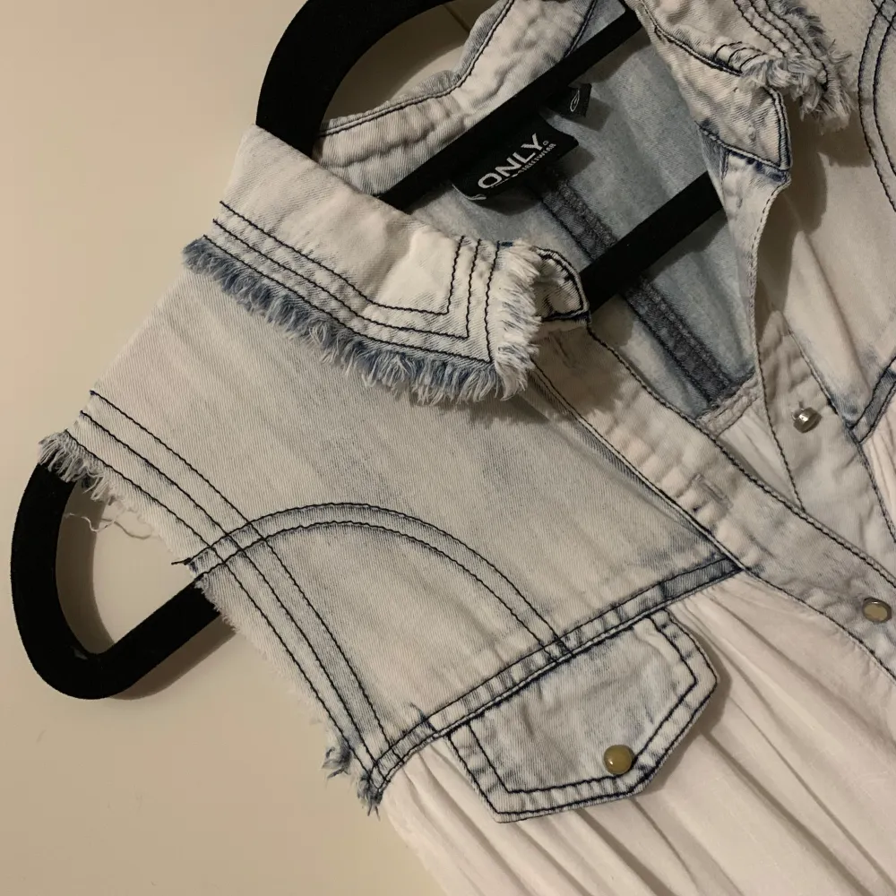 Säljer en vit ärmlös blus från Only med jeansdetaljer. Blusen har en krage och knappar framtill samt två bröstfickor. Perfekt för en avslappnad stil med en touch av denim.. Puserot.