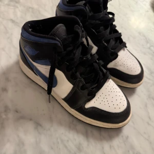 Nike Air Jordans i svart, blå och vit - Säljer ett par Nike Air Jordans i klassisk design med svart, blå och vit färgkombination. Skorna har snörning och en rund tå, perfekt för dig som älskar sneakers med stil. De är både bekväma och trendiga.