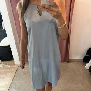 Ljusblå ärmlös klänning - Säljer en stilren ljusblå klänning med en enkel design. Klänningen är ärmlös och har en liten dekorativ detalj vid halsringningen. Perfekt för varma dagar eller sommarens fester.🩵
