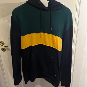 Svart och grön polo hoodie med gul detalj  - Säljer en snygg polo hoodie i svart och grön med en gul rand över bröstet. Knappt använd