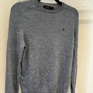 ljus blå  merinoulltröja från Morris - Säljer en stilren ljus blå  tröja från Morris i 100% merinoull. Tröjan har en liten broderad detalj på bröstet och är perfekt för kyligare dagar. Den har en klassisk passform med långa ärmar och ribbade kanter.