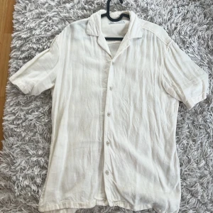  Kortärmad skjorta från Zara Man - Säljer en stilren vit kortärmad skjorta från Zara Man. Skjortan har en klassisk krage och knäppning framtill. Perfekt för varma dagar och ger en avslappnad look. Passar bra till både jeans och shorts.