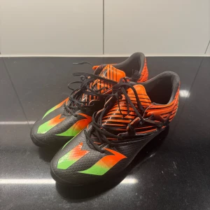 Adidas Messi 15.1 FG/AG - Adidas fotbollsskor Messi 15.1 i svart, orange och grön färg. Skorna är i bra skick och har använts i ca 1 månad. Hör gärna av dig vid eventuella frågor