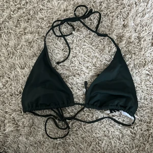 Mörkgrön bikiniöverdel från Weekday - Mörkgrön bikiniöverdel från Weekday. Triangelformad med knytband i nacken och ryggen för justerbar passform. Helt oanvänd då jag köpte flera storlekar. Liten vit fläck på insidan, se bild 3(tror det kommer från ett klistermärke)